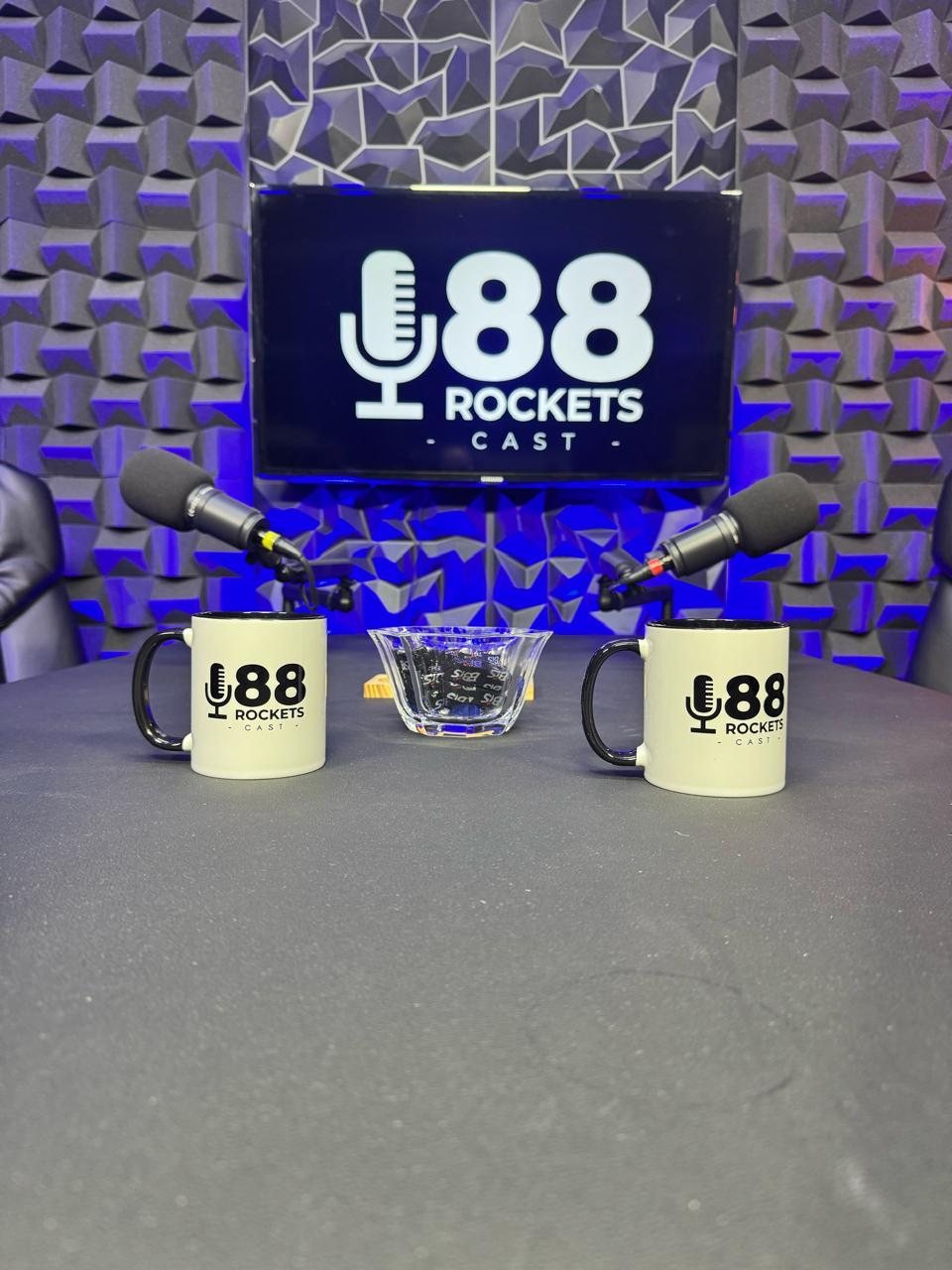 Mesa de gravação do estúdio de podcast em Campinas com microfones e canecas da casa