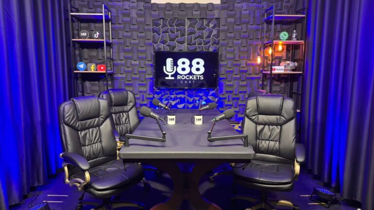 Mesa do estúdio de podcast em Campinas com dois microfones dinâmicos em braço articulado, painel de LED e parede com tratamento acústico